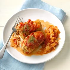 a white plate topped with stuffed cabbage covered in sauce and garnished with herbs