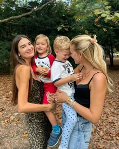 three women and two children are posing for a photo in front of trees with leaves on the ground