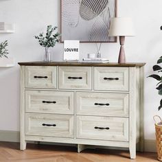 a white dresser sitting next to a potted plant in a living room on top of a hard wood floor