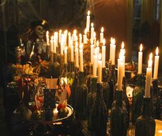 many candles are lit in the middle of a table with wine bottles and other items on it