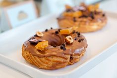 two doughnuts with chocolate frosting and nuts on them sitting on a white plate