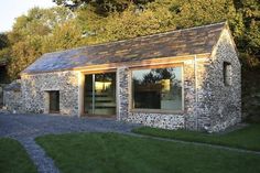 a stone building with windows and grass in the foreground, next to a gravel driveway