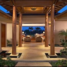 an outdoor walkway leading to a living room and dining area with large wooden pillars on either side