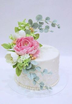 a white cake with pink flowers and green leaves on the top, sitting on a glass plate