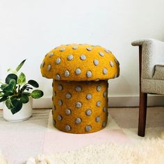 a yellow ottoman sitting on top of a rug next to a chair and potted plant