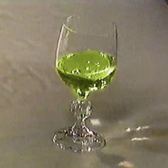 a wine glass filled with green liquid on top of a table