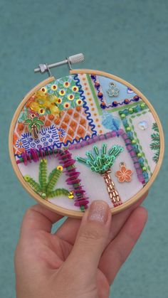 a hand holding a small embroidery kit with palm trees and other things on the hoop