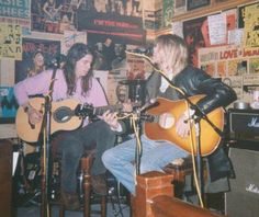 two people playing guitars in a room with posters on the wall