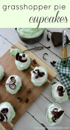 cupcakes with white frosting and chocolate decorations on a cutting board next to a knife