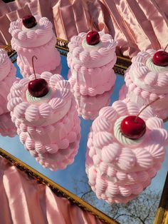 pink cakes with cherries on them are displayed in front of a mirrored table top