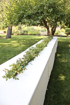 a long white bench sitting on top of a lush green field next to a tree