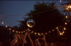 people holding up their hands in the air with disco balls hanging from strings above them