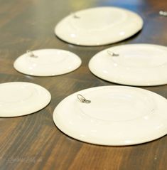 four white plates sitting on top of a wooden table next to each other with silver pins in them