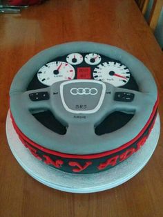 an audi car steering wheel cake with red and white piping on the front, sitting on a wooden table