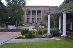 an old building with columns in front of it and flowers growing on the lawn below