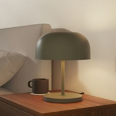 a table lamp sitting on top of a wooden night stand next to a coffee cup