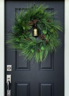 a christmas wreath on the front door of a house with bells and pine cones hanging from it