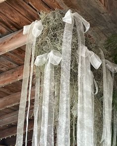 a hanging planter filled with grass and white sheer ribbon on top of a wooden structure