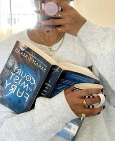 a woman reading a book while drinking from a cup