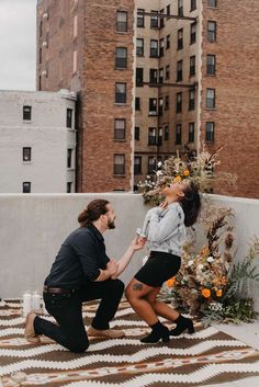 a man kneeling down next to a woman on top of a roof