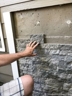 a man sitting on the ground next to a brick wall with his hand reaching for something