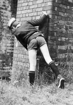 an old photo of a man leaning against a brick wall with his leg in the air