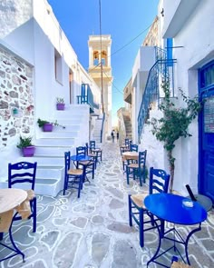 an alleyway with blue chairs and tables on the sidewalk in front of white buildings