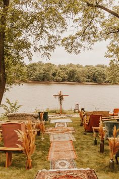 an outdoor wedding setup with chairs and rugs on the grass by the water's edge