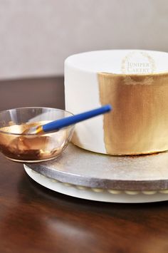 a white cake with gold frosting and a blue handled knife on a plate next to it