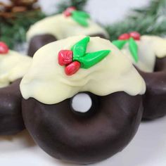 chocolate covered doughnuts with white frosting and holly decorations on them, sitting on a plate