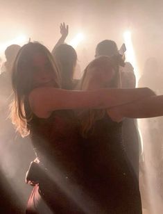 two women are dancing in the dark with their arms around each other and lights shining down on them