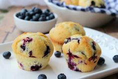 three blueberry muffins on a white plate with some berries in the background