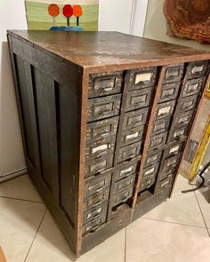 an old wooden cabinet with many drawers on it's sides, in front of a painting