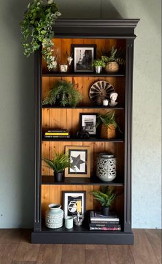 a bookcase with plants and pictures on it in a room that has wood floors