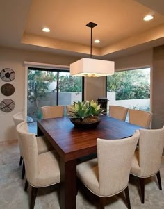 a dining room table with chairs and a bowl on it in front of large windows