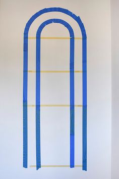 a painting on the wall with blue tape in front of it and an arched window behind it