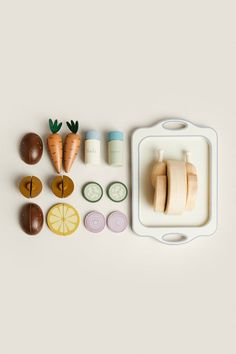 an assortment of fruits and vegetables on a white surface with a cutting board, carrots, garlic, eggs, and other items