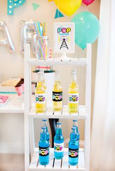 bottles of soda on a shelf with balloons in the background