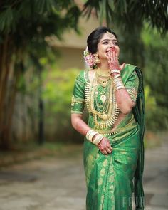 a woman in a green and gold sari with her hands on her face while standing outside