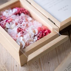 a wooden box filled with flowers on top of a table next to an open book