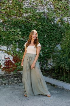 a woman standing in front of a wall with ivy growing on it and smiling at the camera