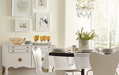 a dining room table with white chairs and gold trimmings on the sideboard