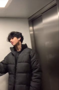 a man in a black jacket standing next to an elevator