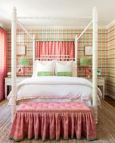 a bedroom with pink and green plaid wallpaper, white bedding, and an upholstered canopy