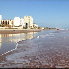 people are walking along the beach in front of some buildings and waves crashing on the sand