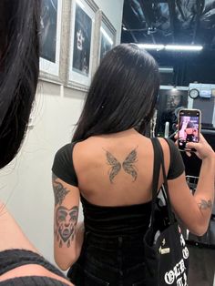 a woman taking a selfie in front of a mirror with tattoos on her back