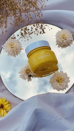 a jar of honey sitting on top of a mirror next to flowers and blue fabric