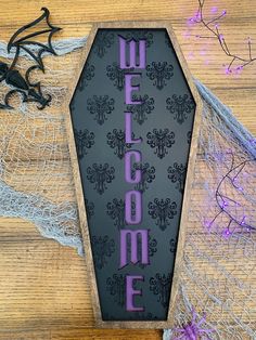 a welcome sign is displayed on a wooden table with purple and black decorations around it