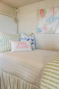 a white bed topped with lots of pillows next to two paintings on the wall behind it