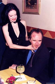 a man and woman sitting at a table with drinks in front of them, posing for the camera